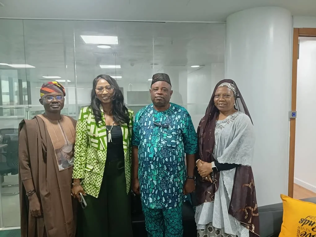 Dr. Alabi in brown Agbada standing with three corporate executives and partners inside a glass-partitioned modern office space.
