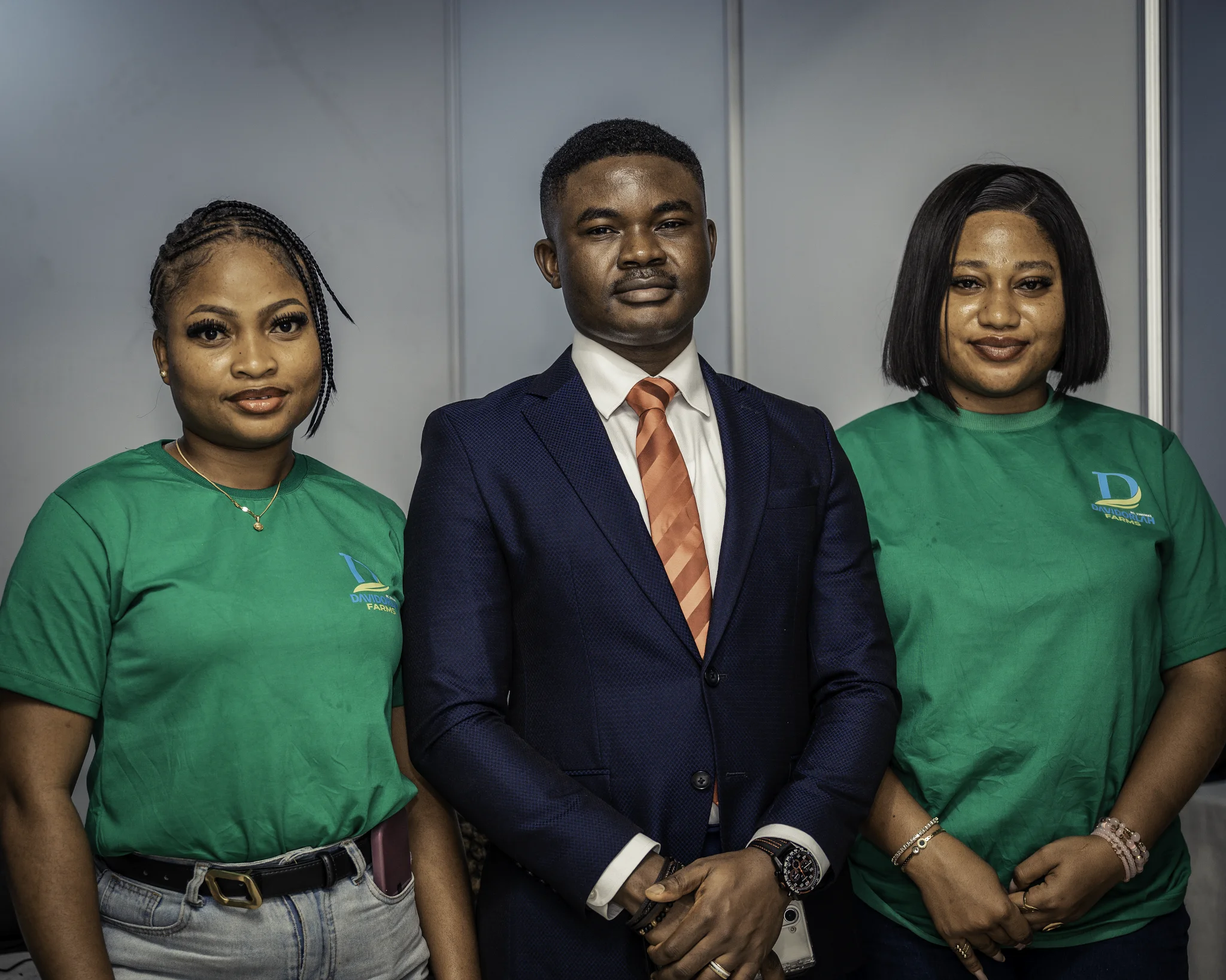 Dr. Alabi in a dark suit standing proudly between two female team members dressed in branded green Davidorlah Farms t-shirts.