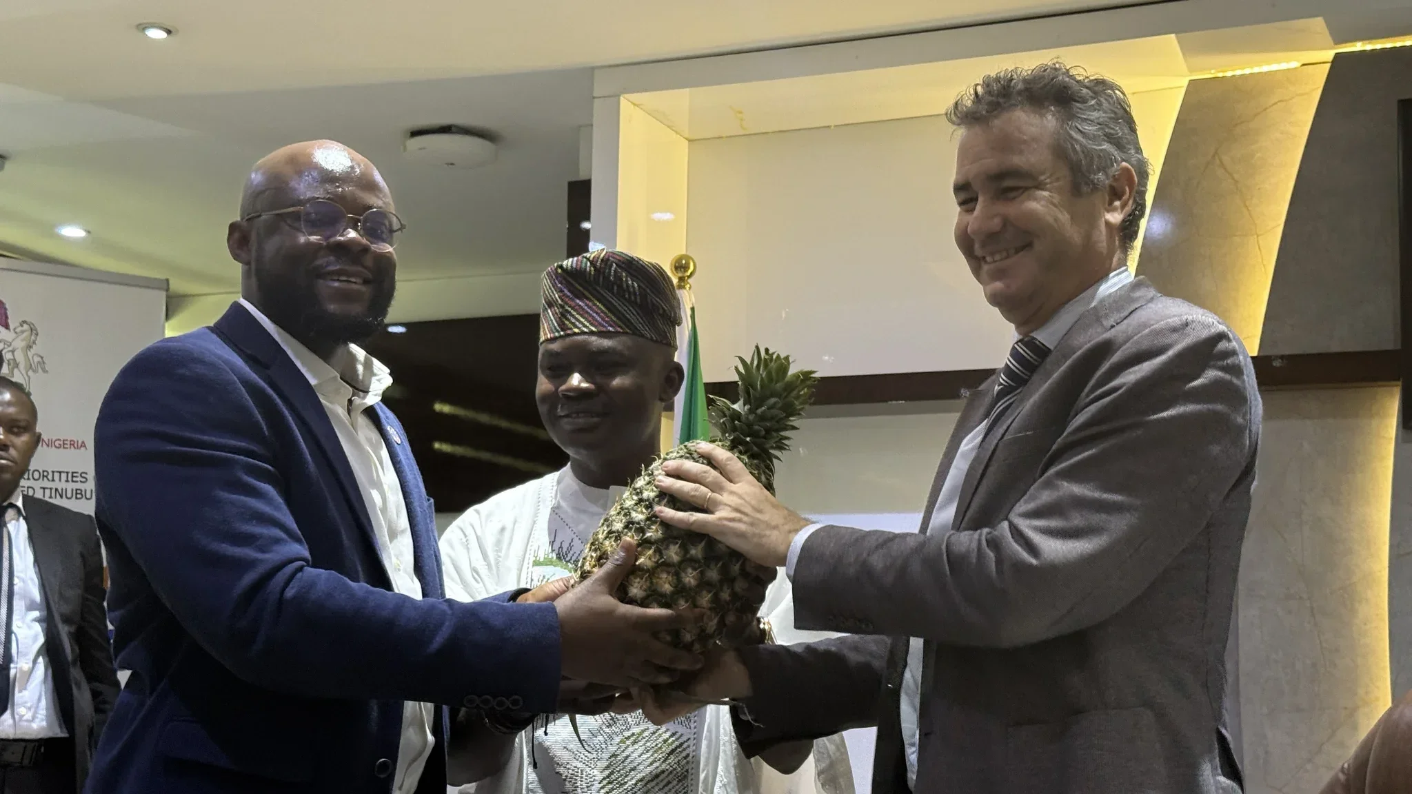 Dr. Alabi standing between two international corporate delegates as they jointly examine a fresh, export-grade pineapple.