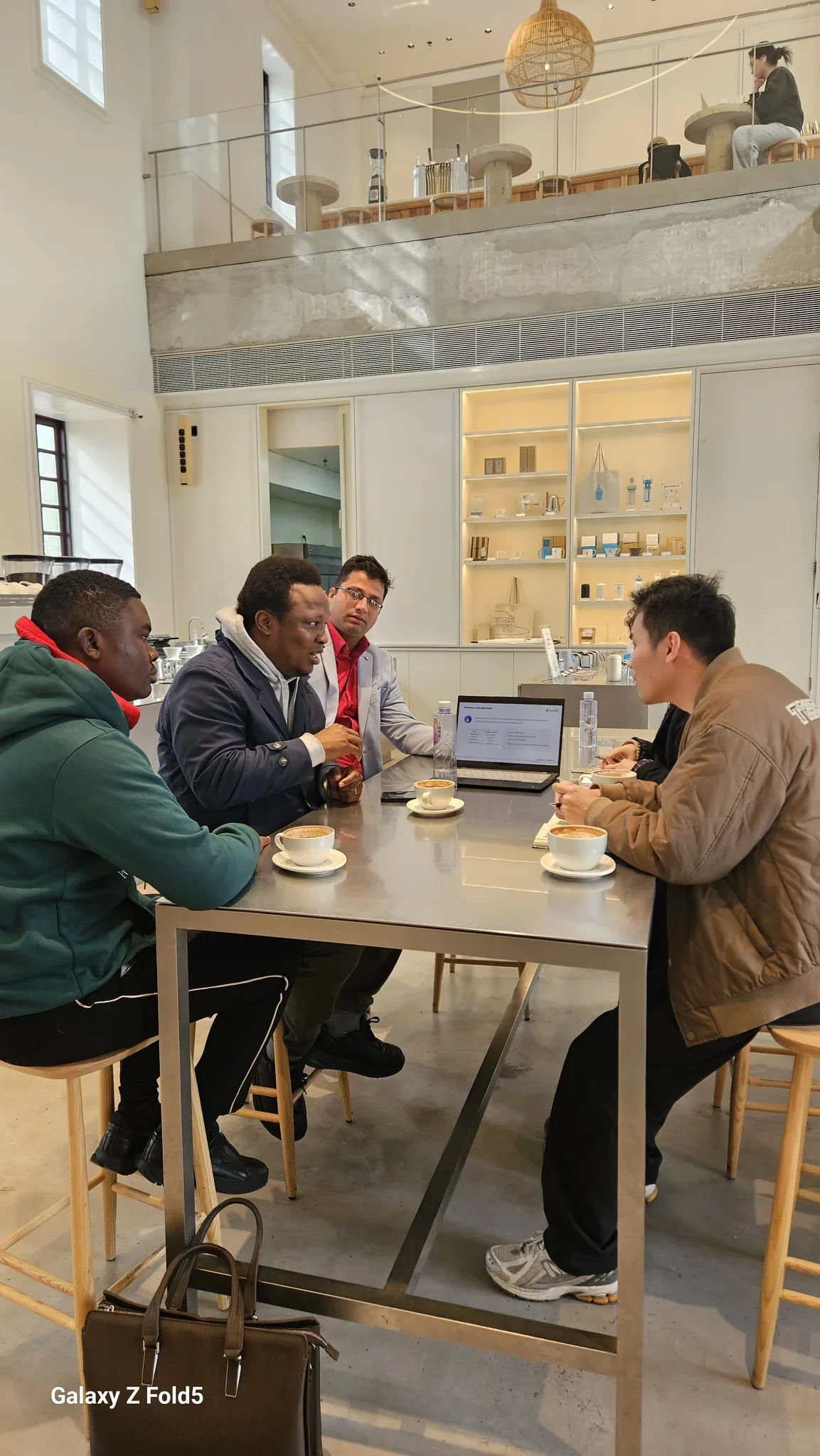 Dr. Segun Alabi seated at a high coffee table during an international trade discussion with a panel of four foreign delegates reviewing laptop data.
