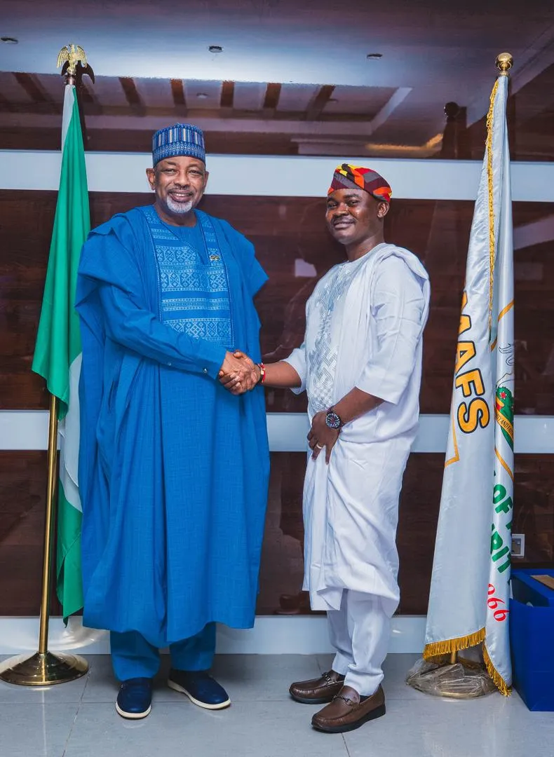 Dr. Alabi shaking hands with the Minister of Agriculture and Food Security, Senator Abubakar Kyari, in front of the official national and ministry flags.