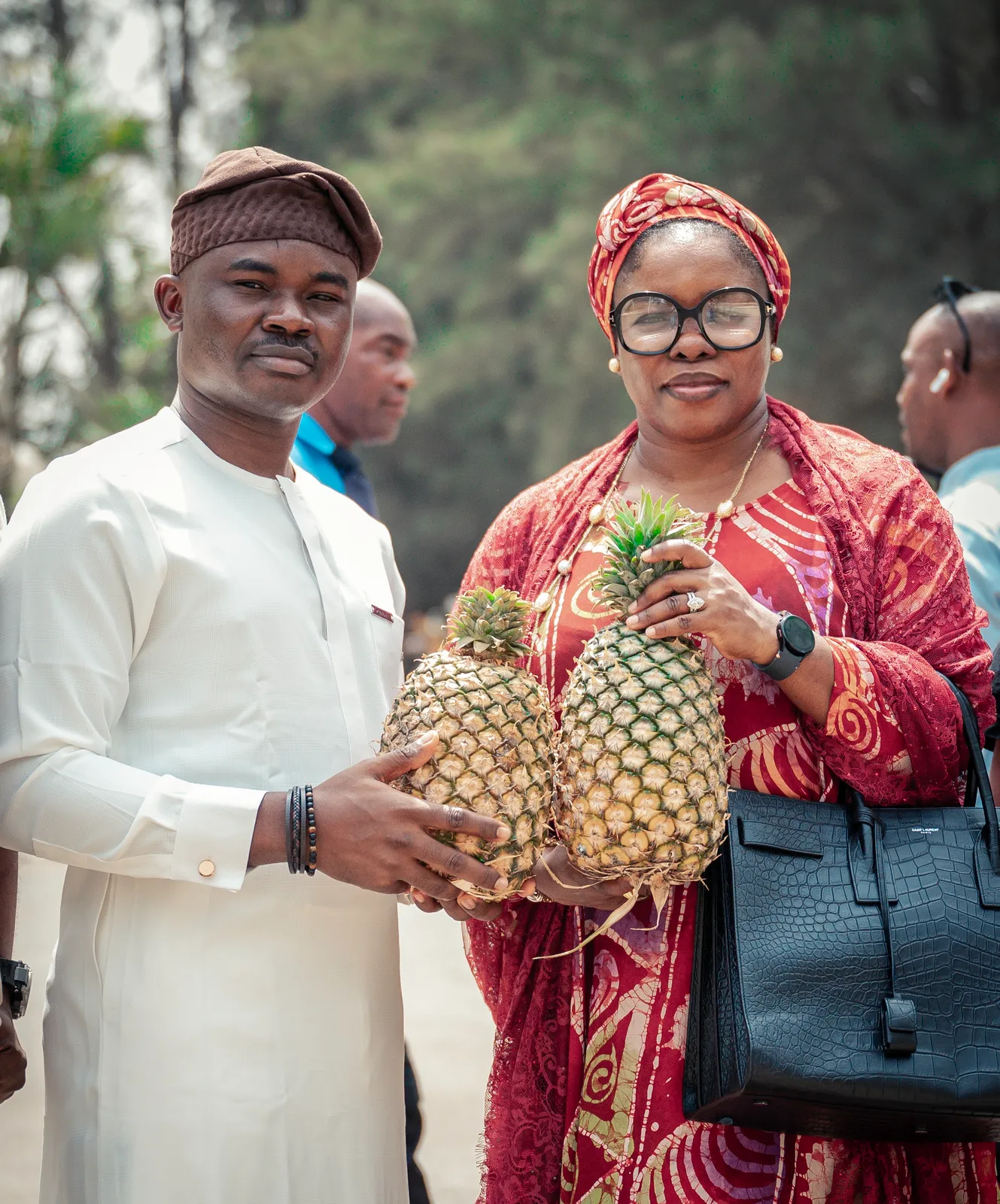Dr. Alabi and a senior partner holding two large, freshly harvested pineapples outdoors.
