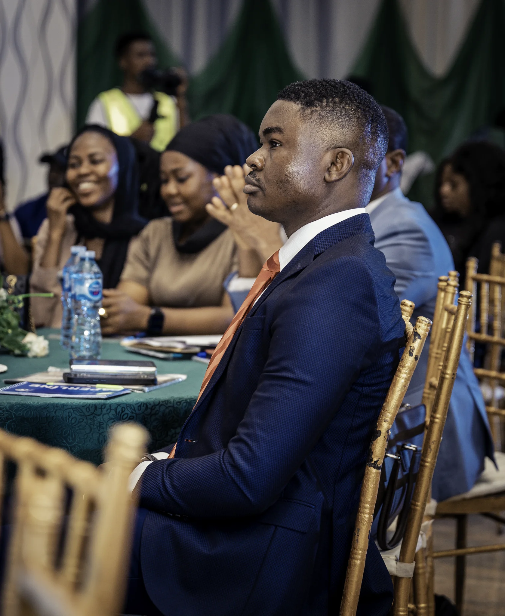 Side profile of Dr. Alabi seated attentively at a round table during a high-level conference session with other attendees in the background.